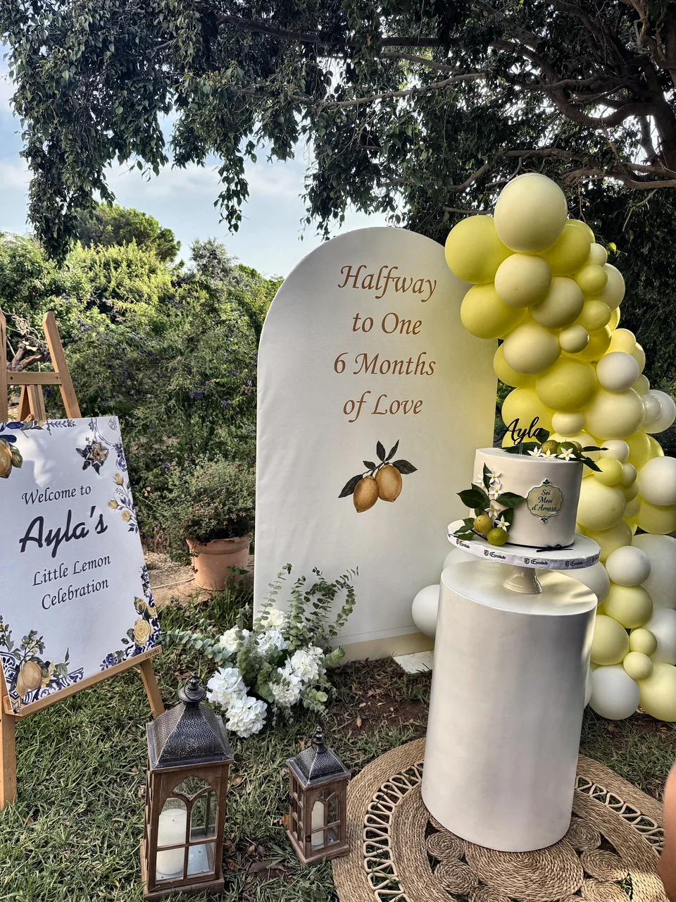 Halfway to One half birthday setup with a lemon yellow balloon garland, a welcome sign and a white cake plinth
