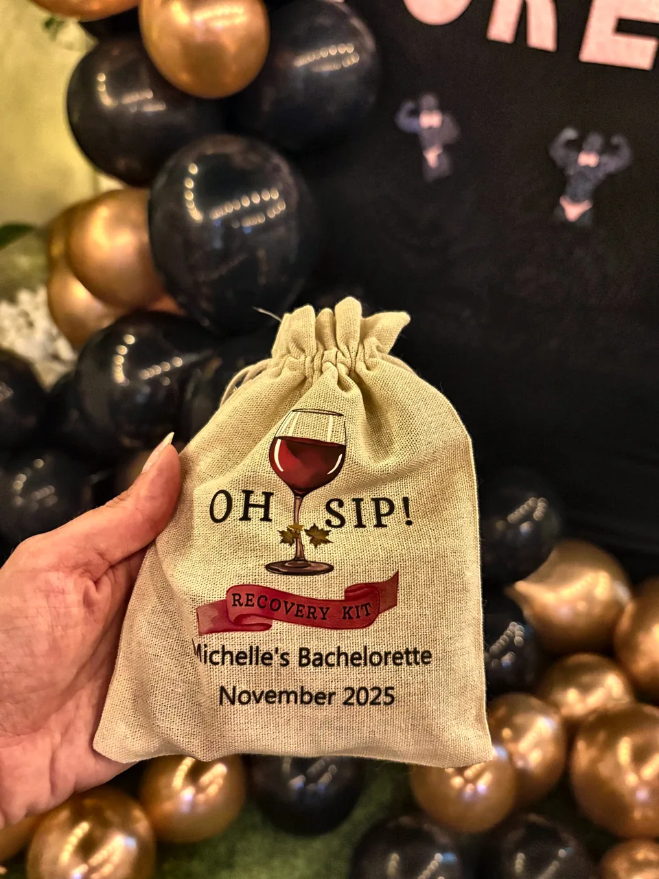 Personalised Oh Sip recovery kit bag for Michelle's bachelorette, held in front of black and gold balloons