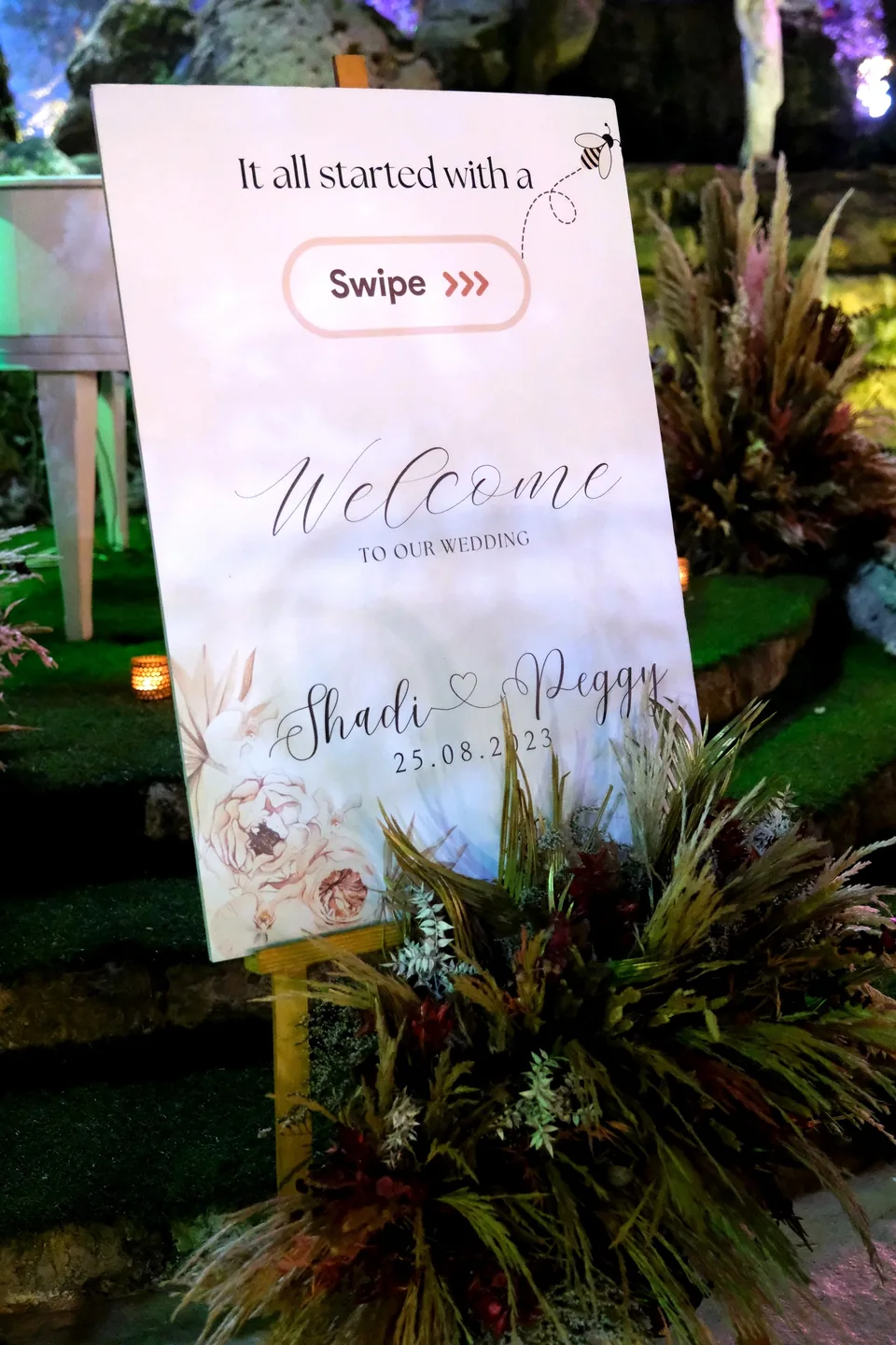 Wedding welcome sign reading It All Started With a Swipe, framed by dried florals
