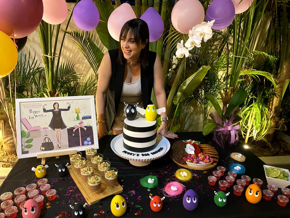 Guest of honour smiling beside her egg shower table with a striped cake and colourful egg characters
