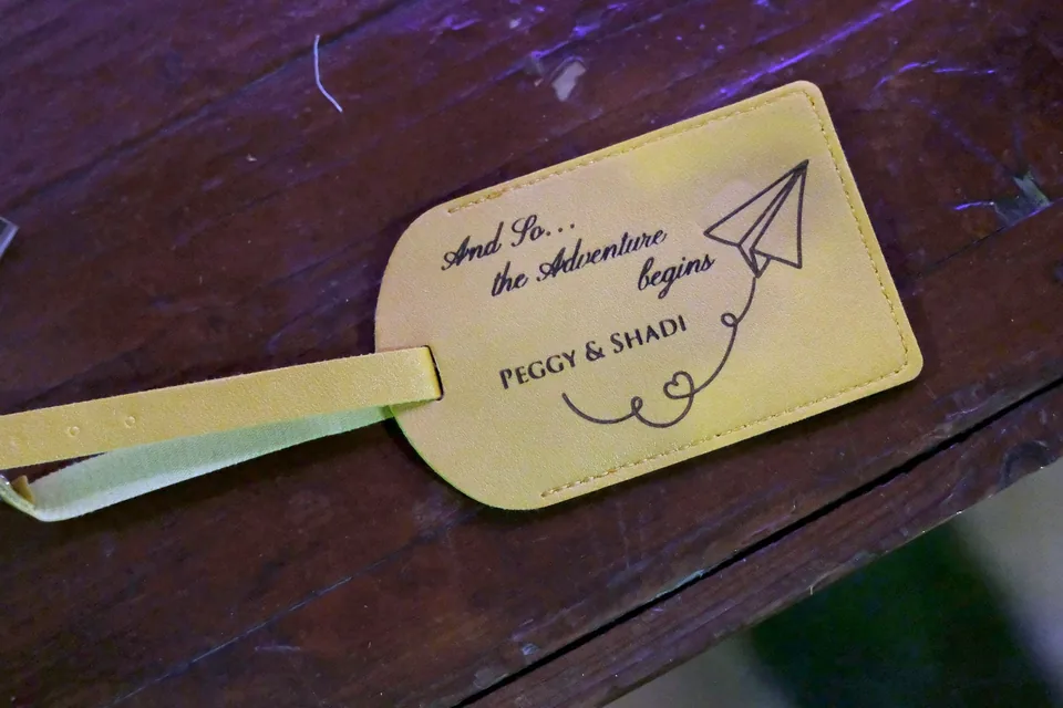 Personalised luggage tag favour for a wedding, reading And So the Adventure Begins