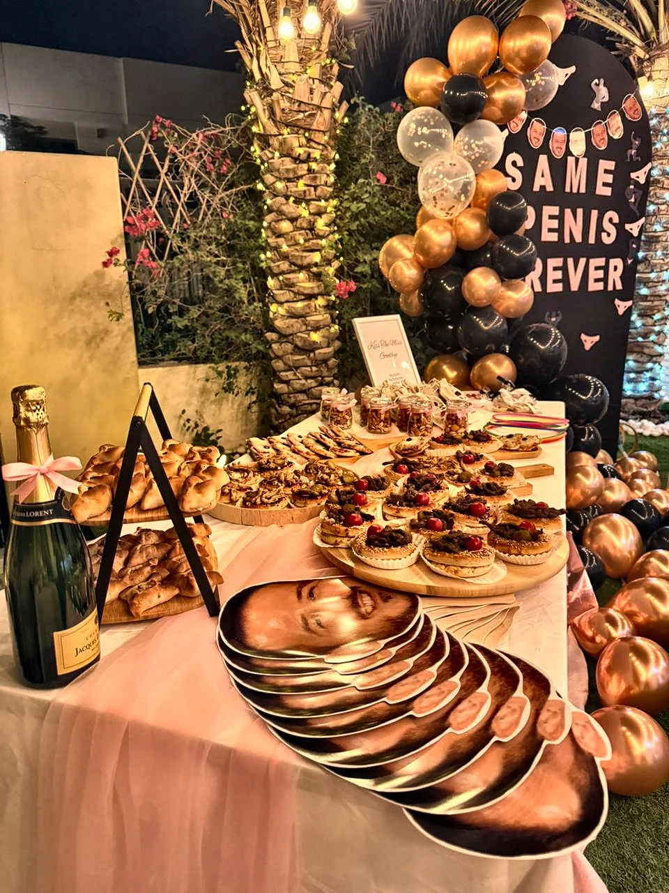 Bachelorette dessert table with pastries and tarts, a stack of groom face masks and gold and black balloons