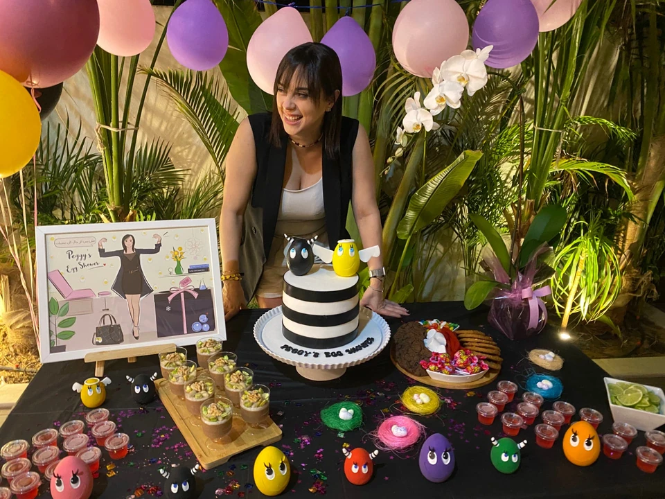 Peggy smiling behind her Egg Shower table with a striped cake, egg characters and her personalised illustration
