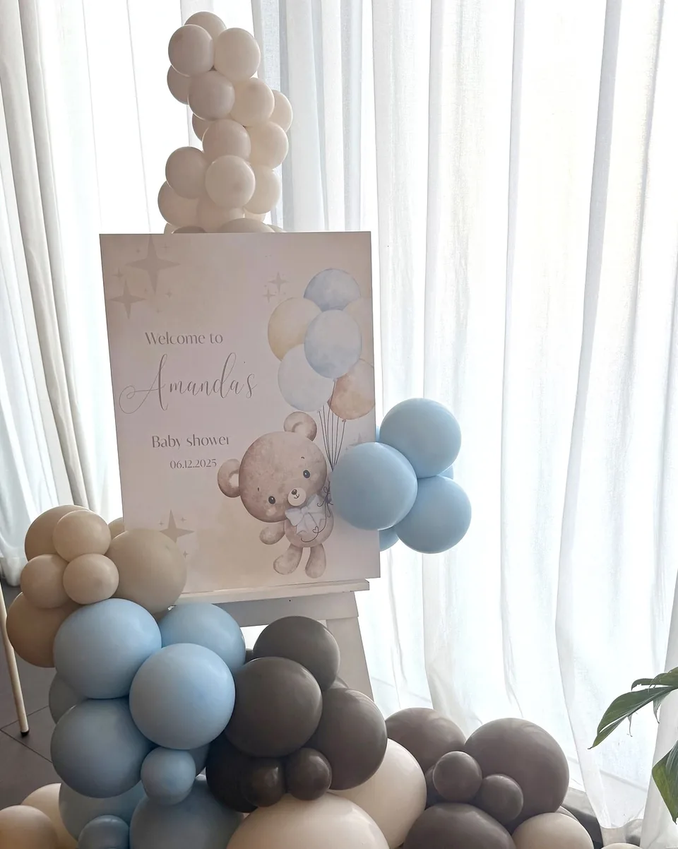 Baby shower welcome easel with blue, taupe and white balloons and a teddy bear illustration