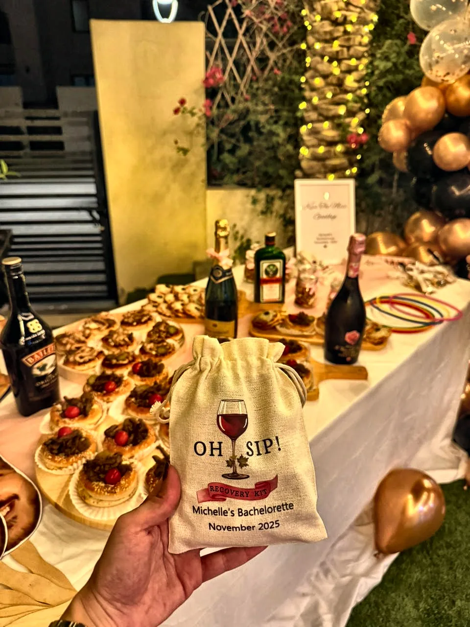 Oh Sip recovery kit favour bag held over a bachelorette dessert table with tarts and bubbly