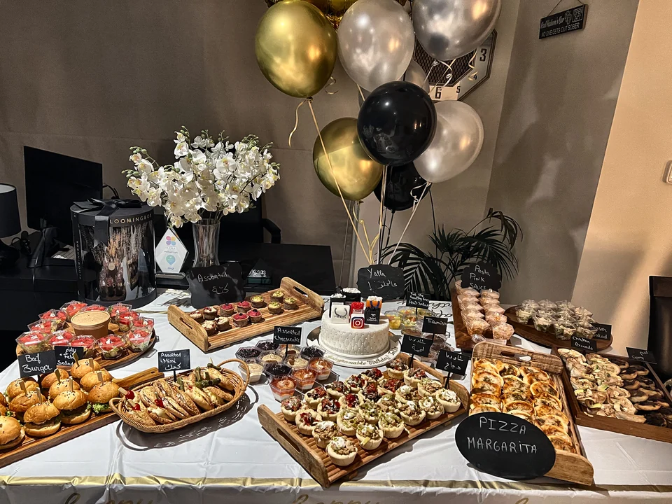 Birthday buffet with black, gold and silver balloons, white orchids and labelled platters