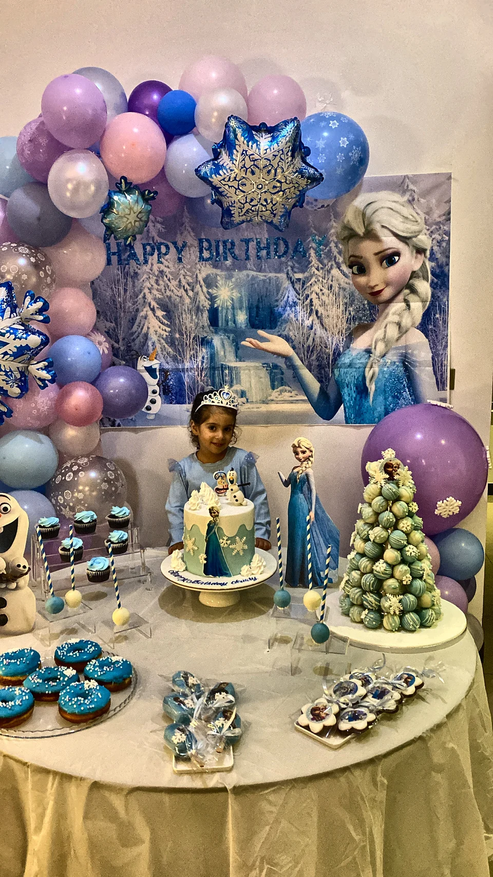 Frozen themed birthday table with a snowflake balloon garland, a princess backdrop and blue treats