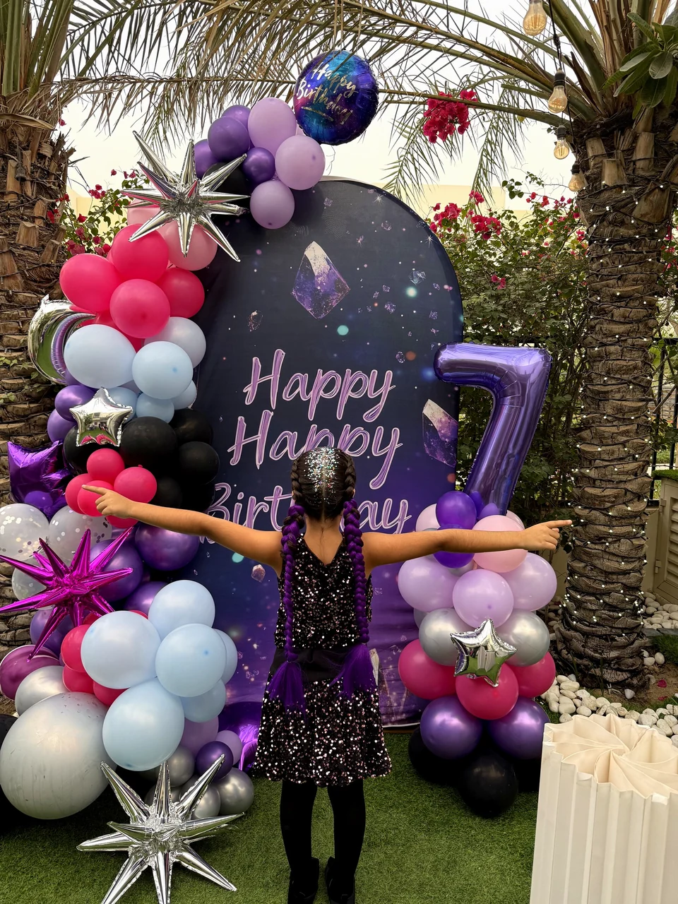 Birthday girl with her arms wide open in front of her purple and pink Happy Birthday backdrop