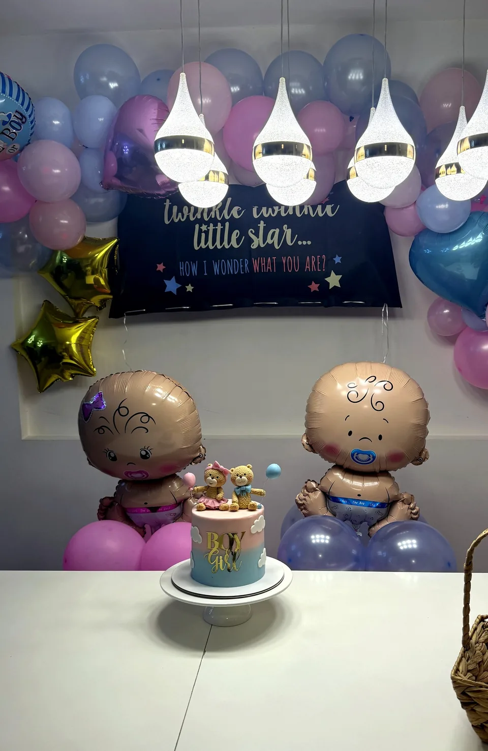Gender reveal setup with a Twinkle Twinkle Little Star backdrop, baby balloons and a small cake