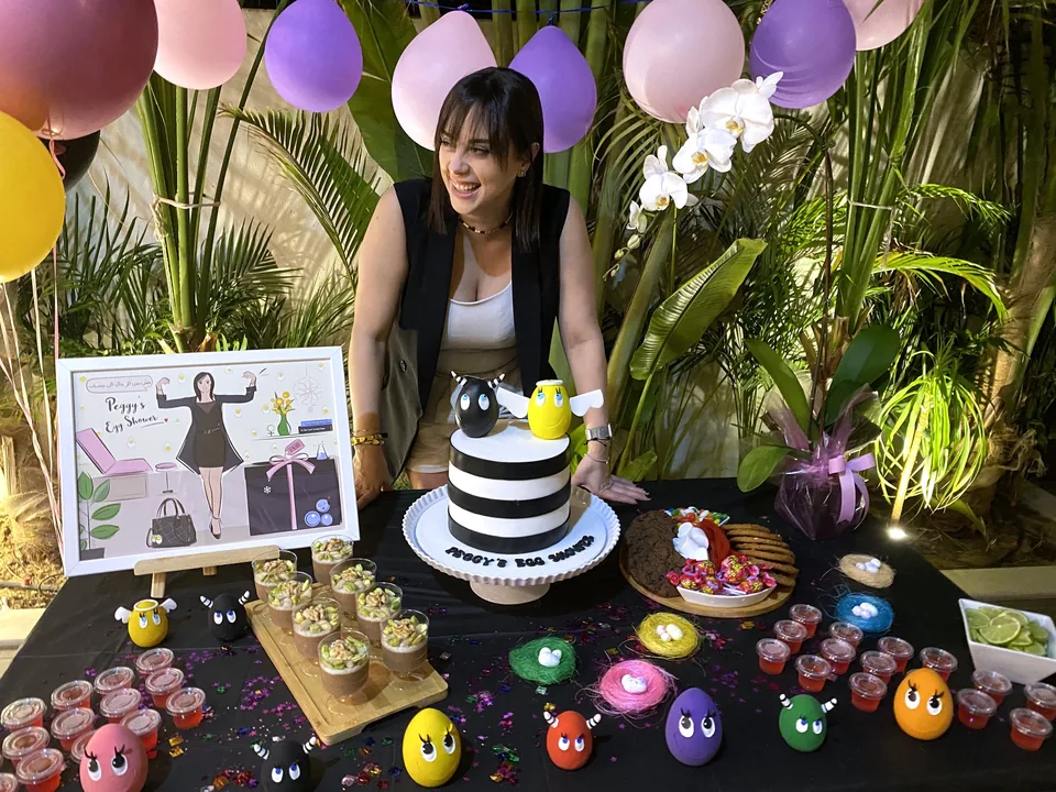 The founder smiling behind her Egg Shower table with a striped cake, colourful egg characters and her personalised illustration